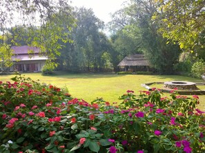 A garden with a thatched-roof structure, a lawn, and flowering plants. - Bulun Buri Resort (Hang Dong)