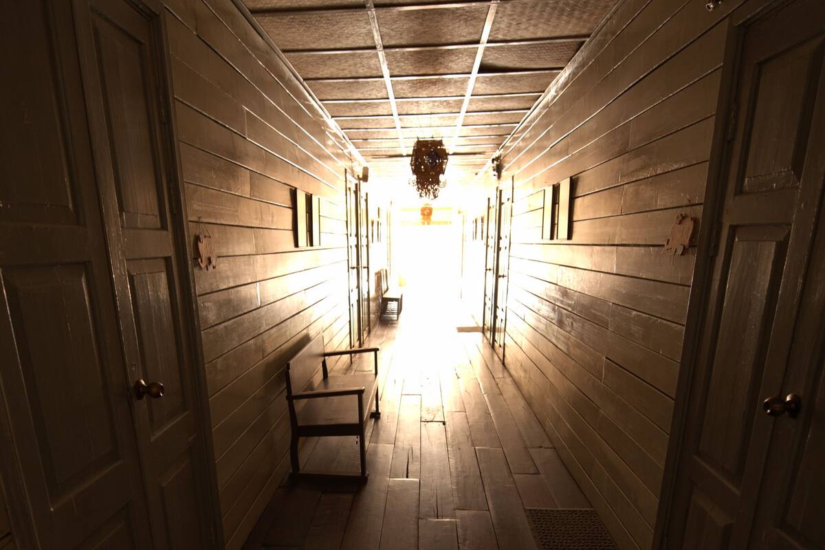 A narrow hallway with wooden walls and doors, leading to a bright area at the end.