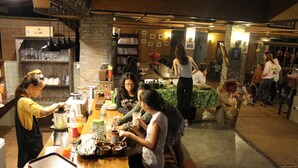 A group of people gathered around a wooden table in a cozy, rustic setting with brick walls and shelves filled with kitchenware. - Bulun Buri Resort (Hang Dong)