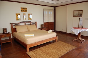A bedroom with a wooden bed, a nightstand, a bedside table, a window with curtains, and a painting on the wall.