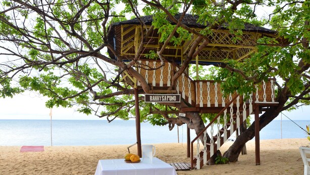 Uma cabana de praia chamada "Bahay Sapuno" com uma mesa e uma saladeira de frutas.