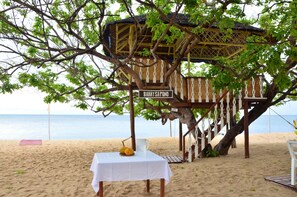 Una cabaña en la playa llamada "Bahay Sapuno" con una mesa y un frutero.