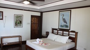 Um quarto com cama de madeira, uma mesinha de cabeceira, um banco de madeira e duas imagens emolduradas na parede.