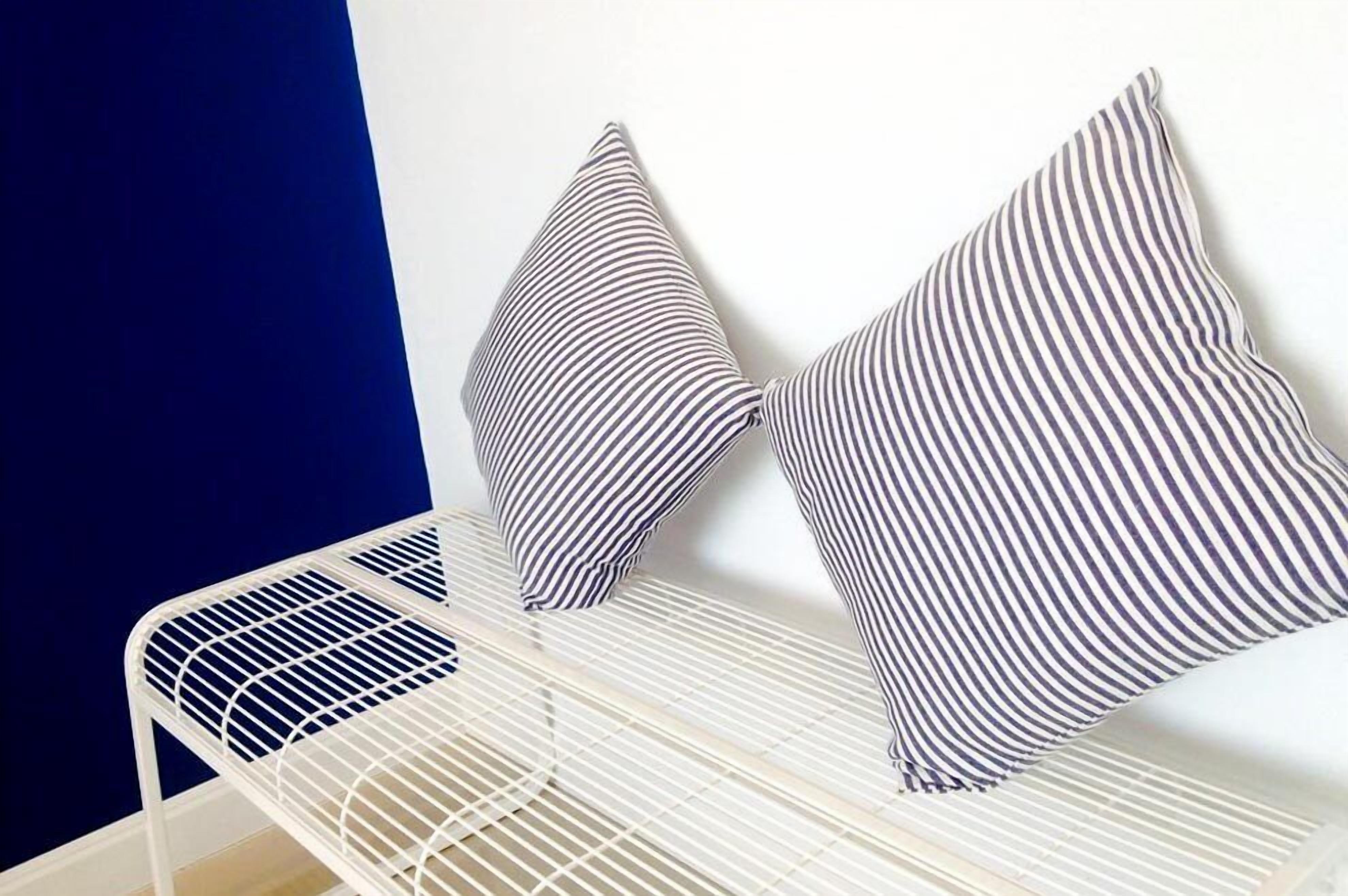 Estructura de cama blanca de metal con dos almohadas a rayas frente a una pared azul y blanca.