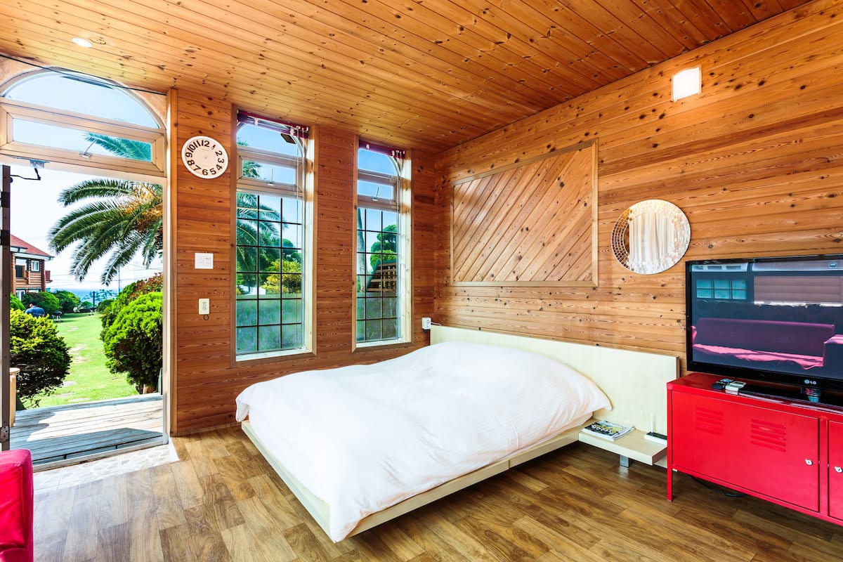 A wooden-paneled bedroom with a bed, a TV, and a red cabinet.
