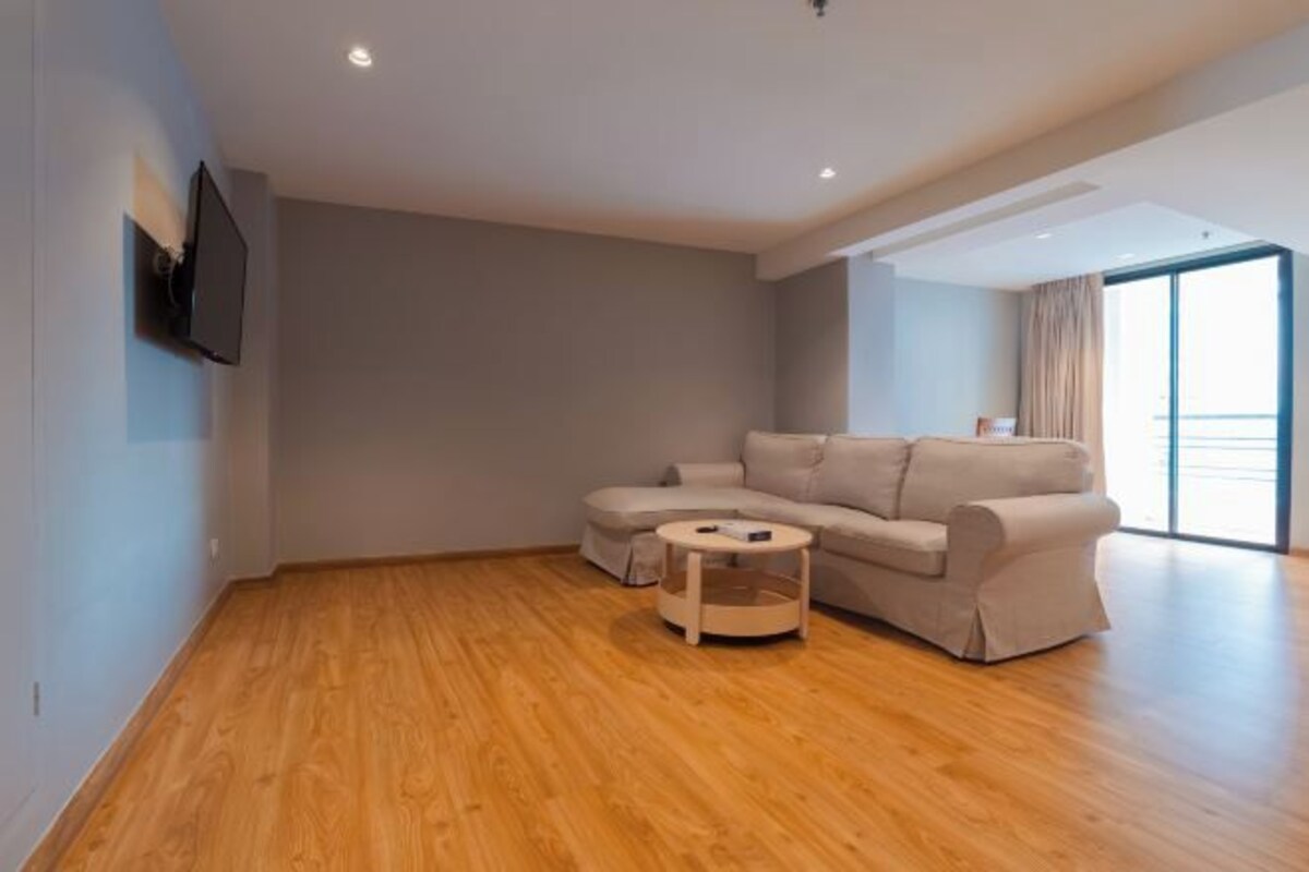 A modern living room with a beige sofa, a small wooden coffee table, and a flat-screen TV mounted on the wall.