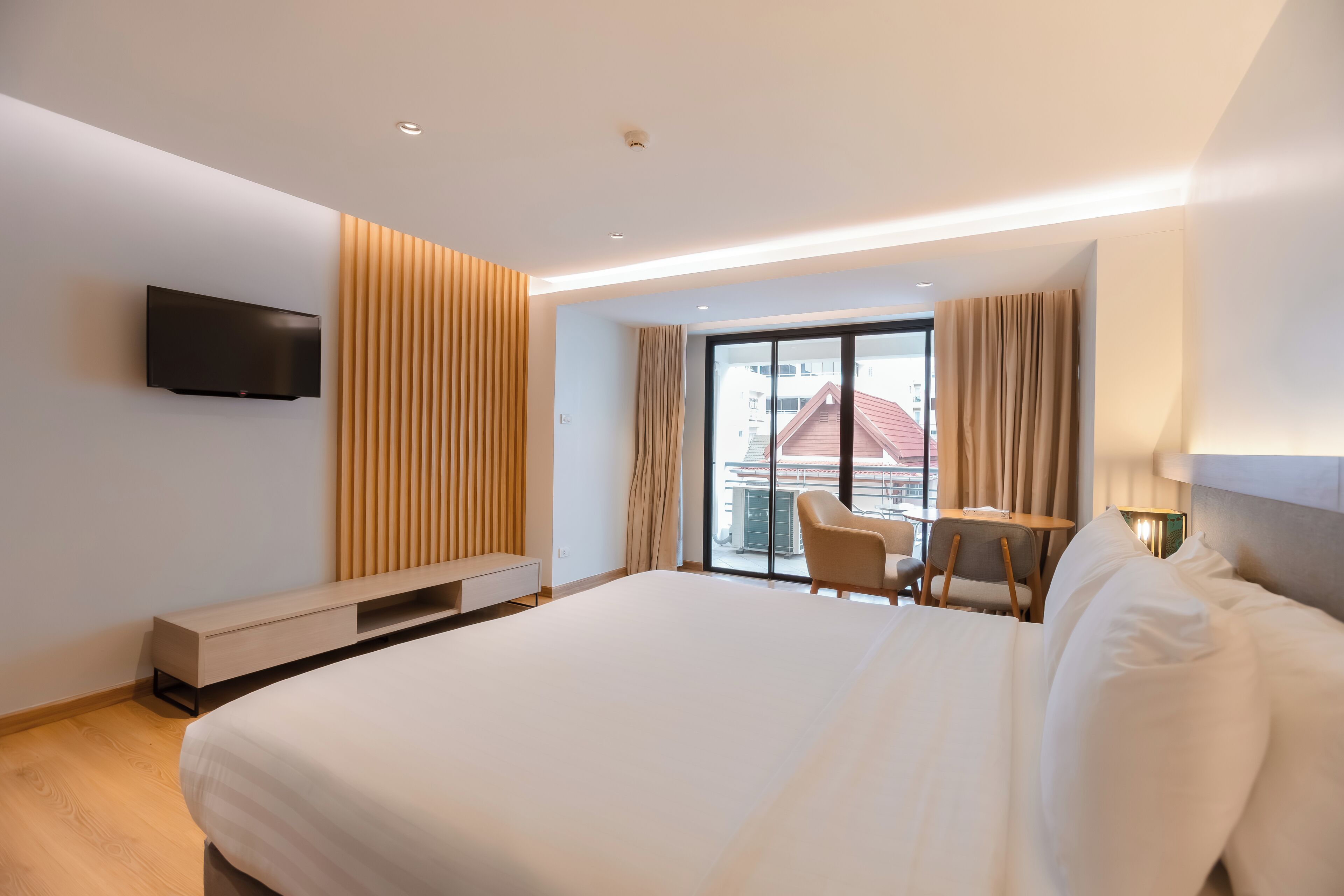 Habitación de hotel moderna con una cama grande, televisión montada en la pared, zona de estar con mesa y sillas, y balcón con vistas.