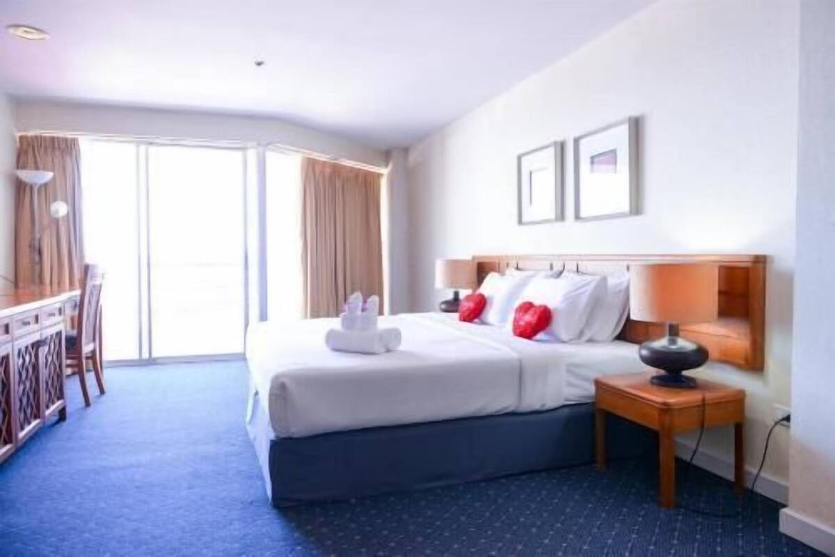 A hotel room with a bed, a desk, a chair, a nightstand, and a window.