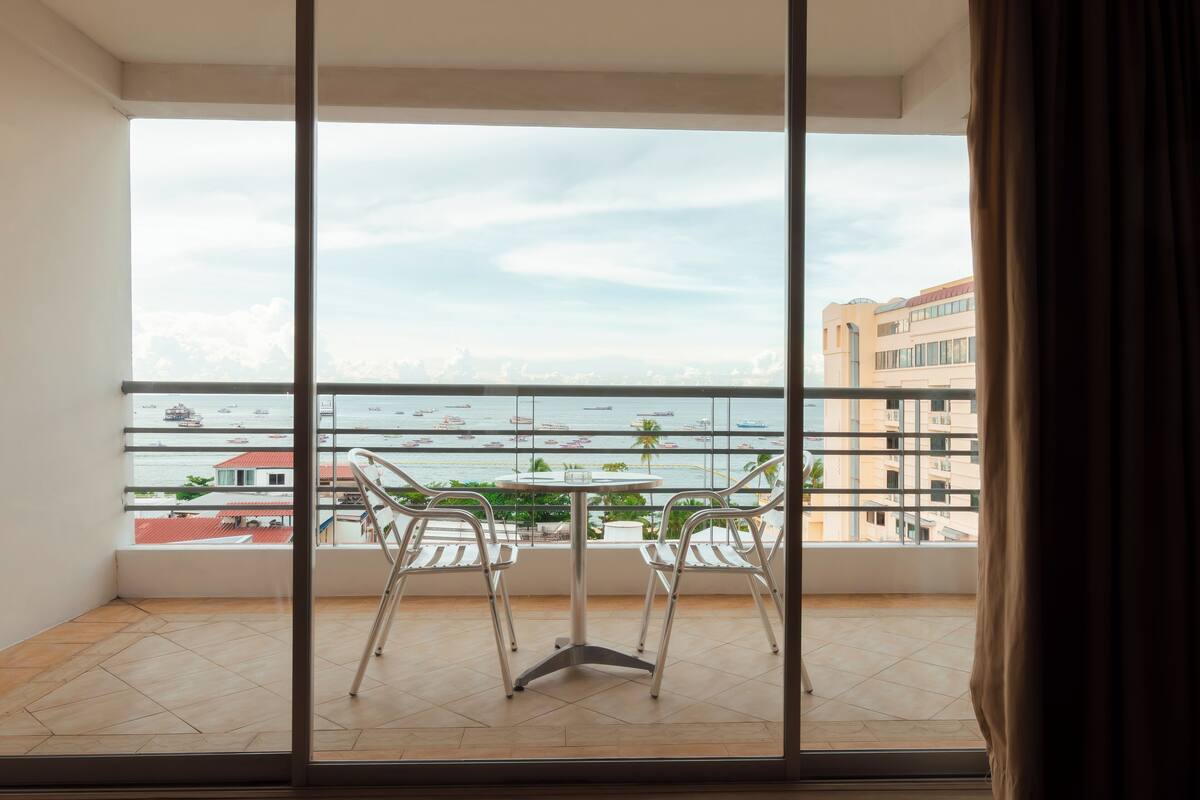 A balcony with two chairs and a table, overlooking a marina with boats and buildings in the background.