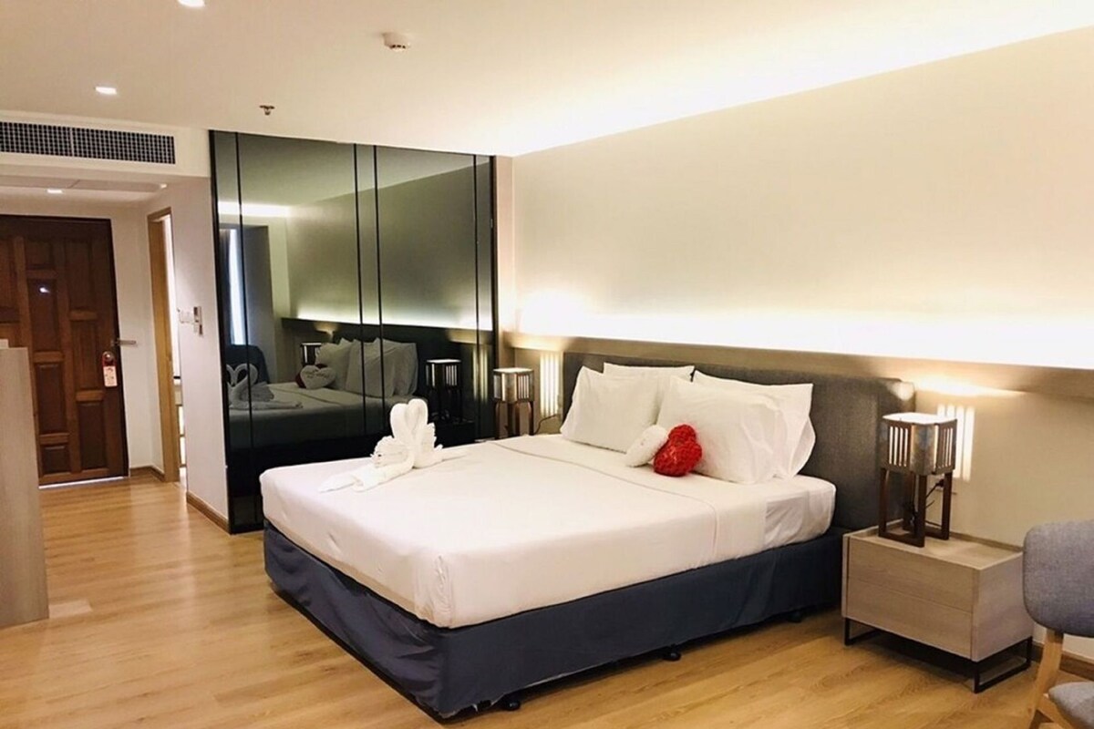 A modern hotel room with a large bed, bedside tables, a mirror, and a wooden floor.