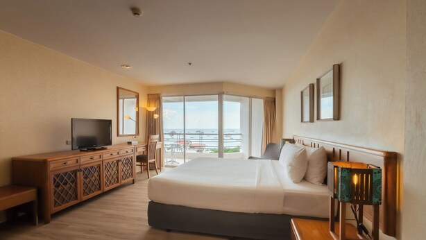 A hotel room with a large bed, a TV, a wooden cabinet, a desk, and a view of the sea. - Sandy Spring Hotel (Pattaya)