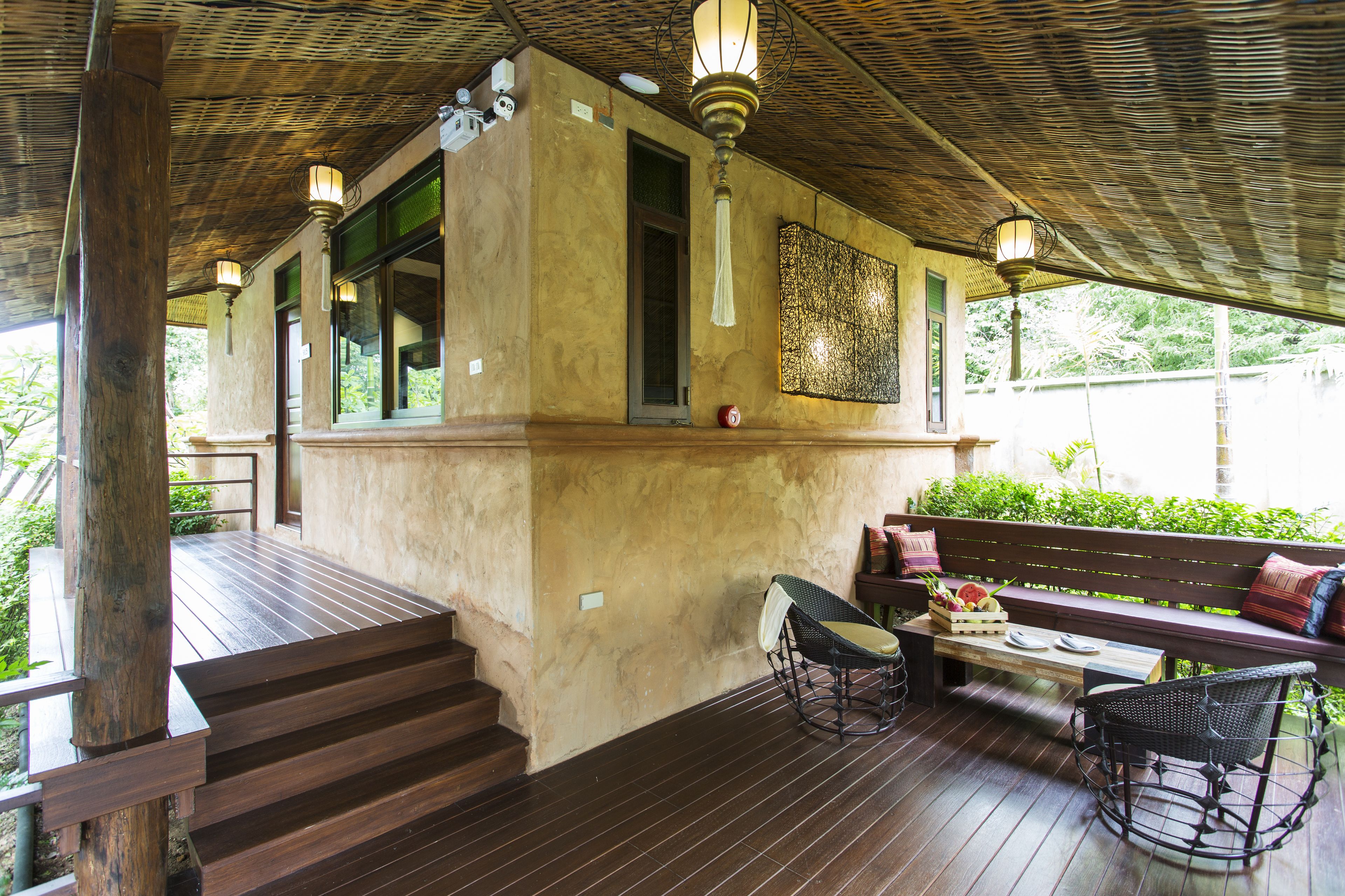 A covered outdoor area with wooden flooring, a bench, a table, and a chair.