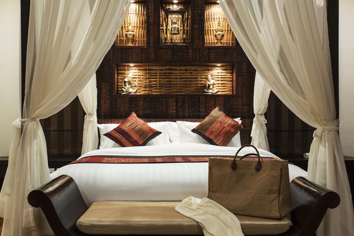 A bed with white linens, two pillows, and a brown bag on a bench.