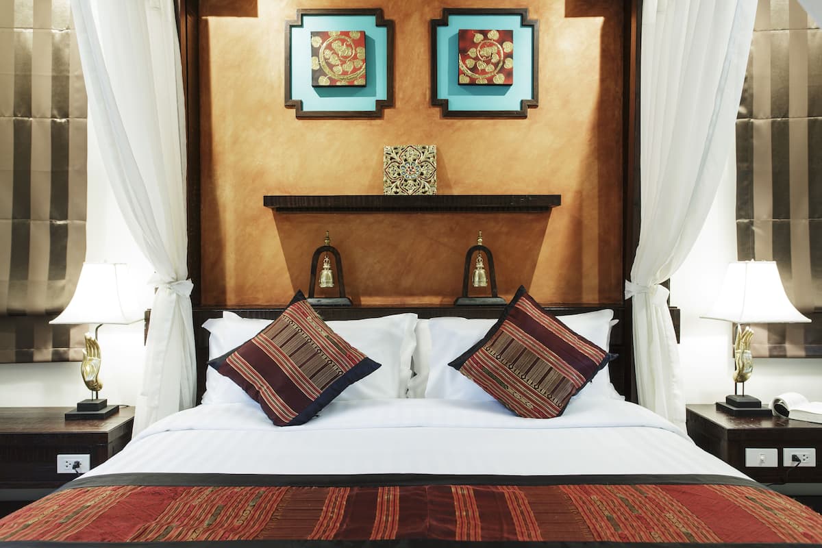 A hotel room with a bed, two bedside lamps, a nightstand, a decorative wall piece, and a window with curtains.