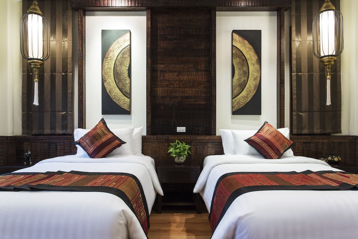 A hotel room with two beds, a dark wood headboard, wall-mounted sconces, and a large mirror.