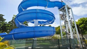 A multi-level blue water slide structure with a metal support tower. - Résidence Tropicale (Le Moule)