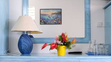 A bathroom with a blue vanity, a mirror, a lamp, a small stool, and a vase with flowers.