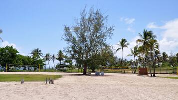 A beach volleyball court with net, sand, and palm trees.