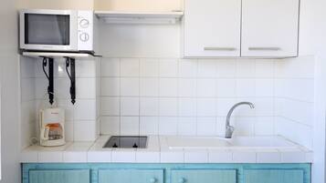 Una cocina con baldosas blancas, microondas integrado, cafetera, lavamanos y armarios color aguamarina con diseños de conchas.
