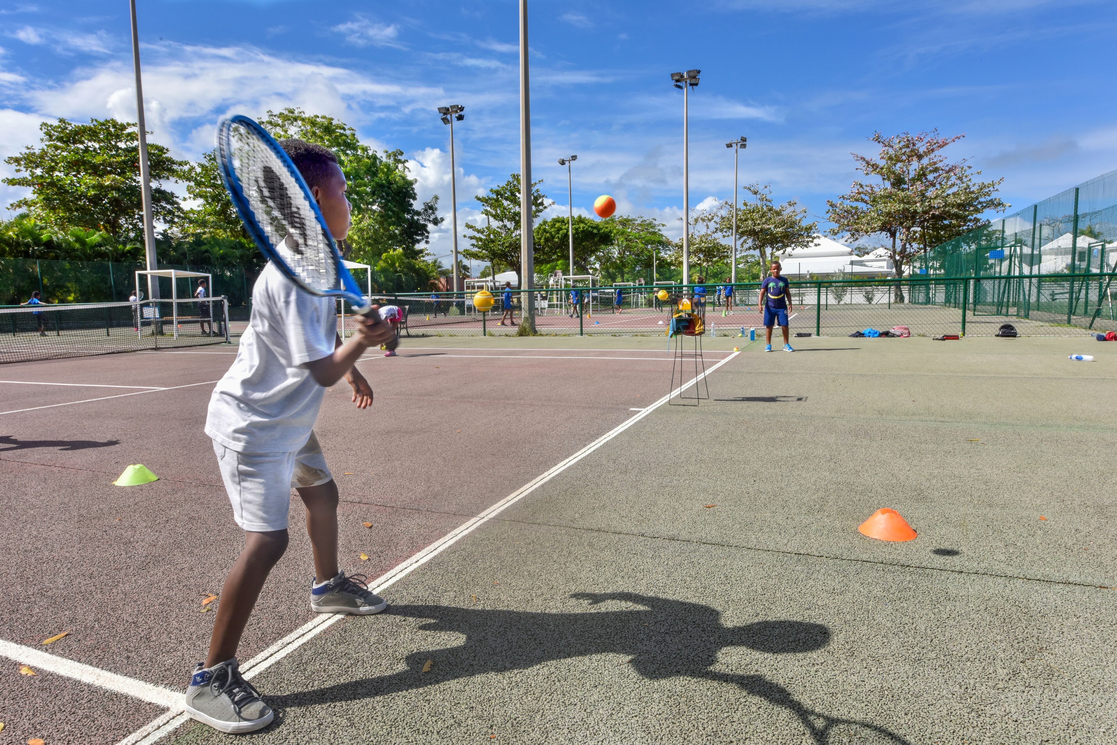 Un court de tennis avec un filet, des cônes verts et des joueurs.