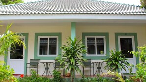 Uma casa com telhado de cerâmica, molduras de janela verdes e um pequeno pátio com duas mesas e cadeiras.