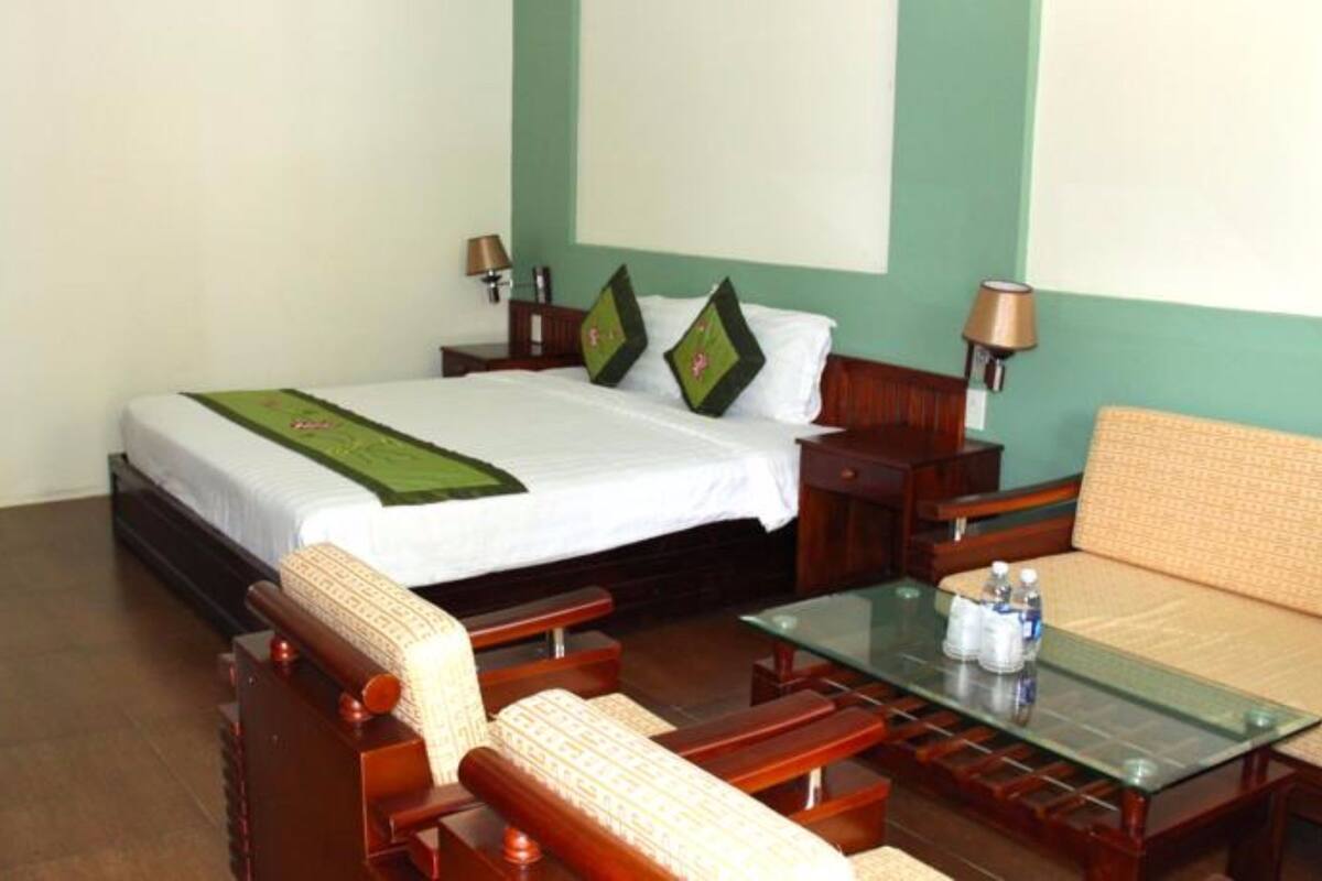 A hotel room with a bed, a glass-top table, a sofa, and a wooden chair.