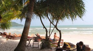 A beach with palm trees, lounge chairs, and a view of the ocean.