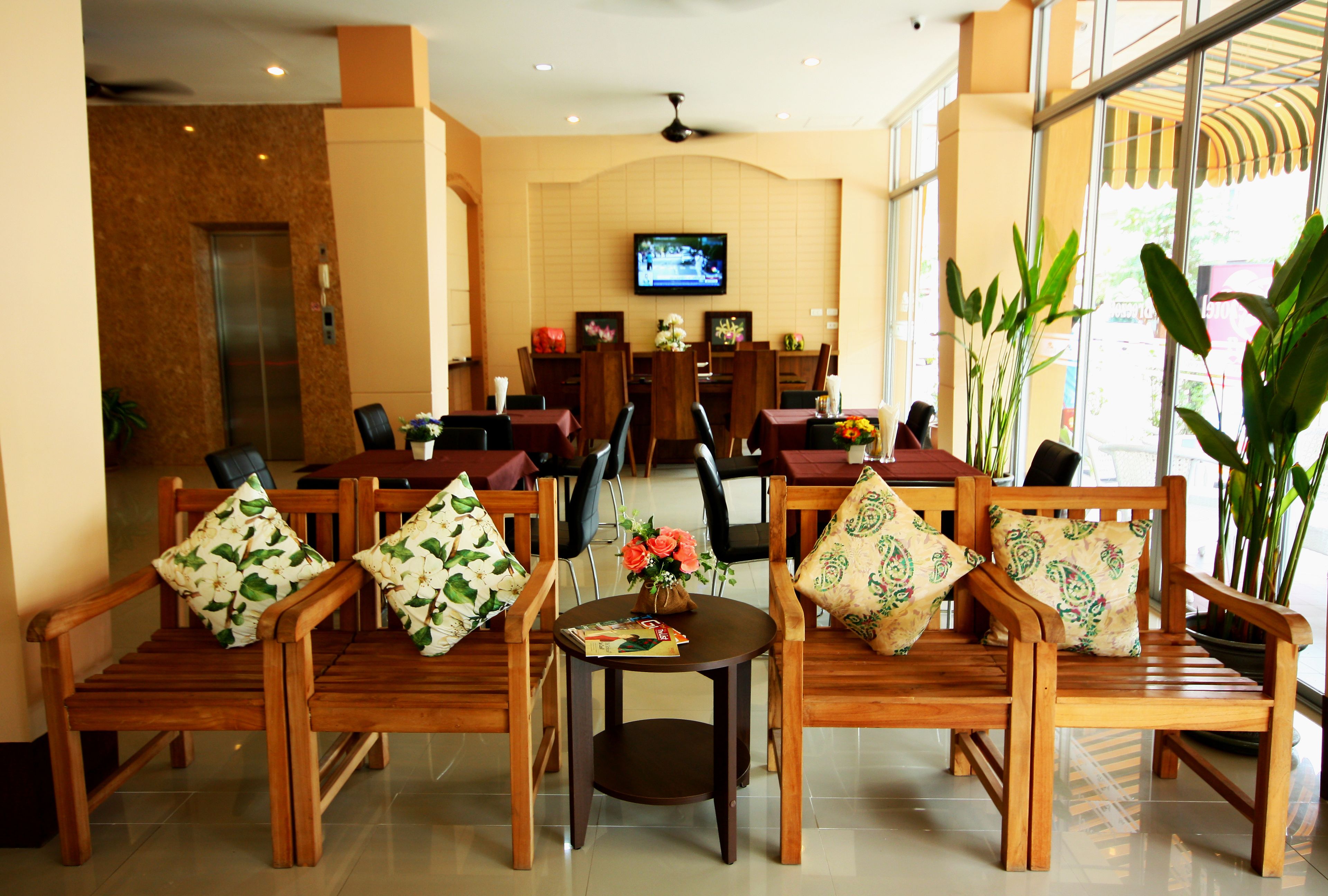 A hotel lobby with wooden furniture, a television on the wall, and potted plants.
