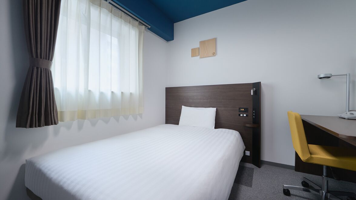 Une chambre d’hôtel équipée d’un lit, d’un bureau, d’une chaise, d’une lampe et d’une fenêtre avec des rideaux.