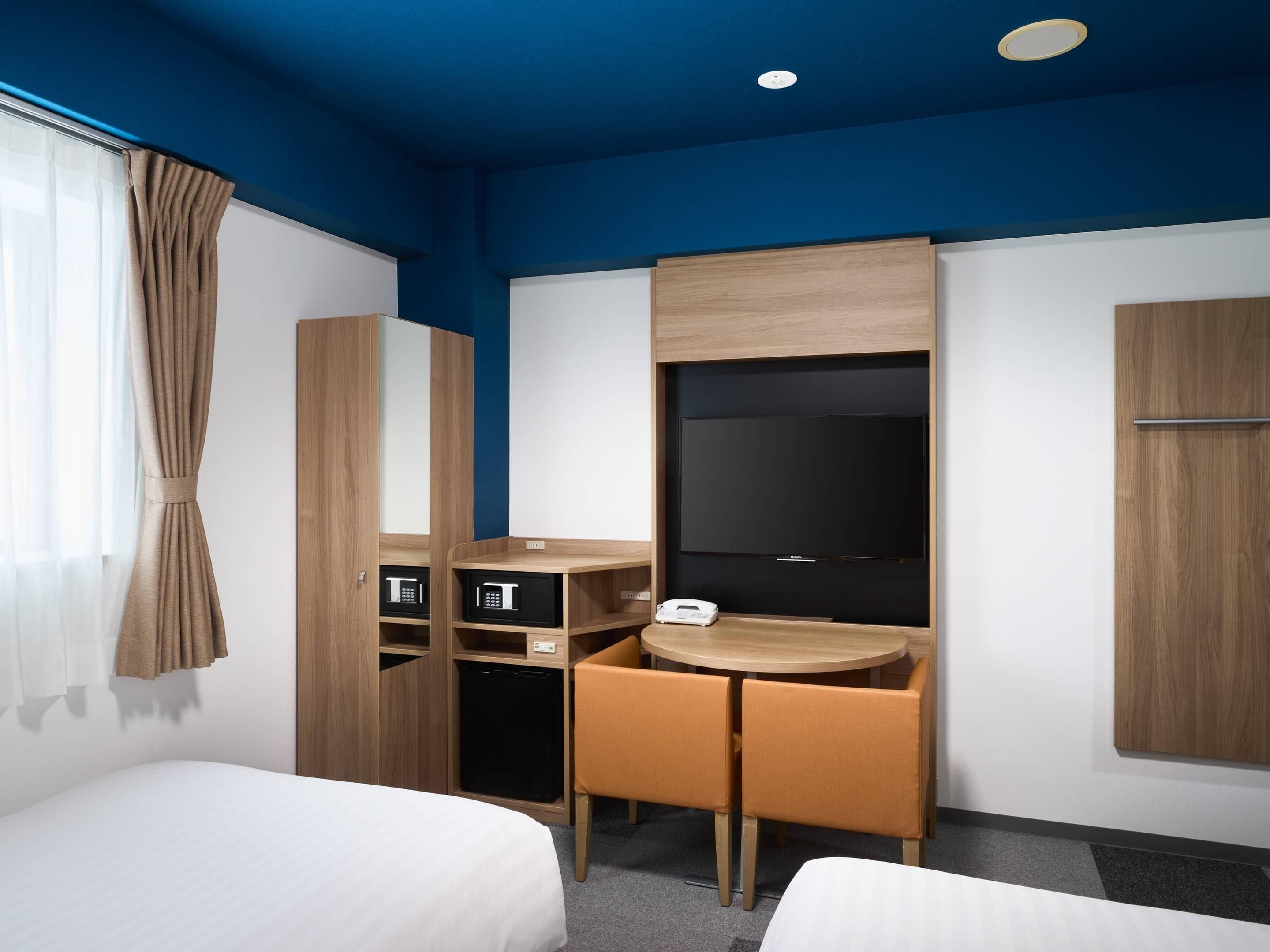 A hotel room with two beds, a desk with a chair, a television, and a wardrobe.