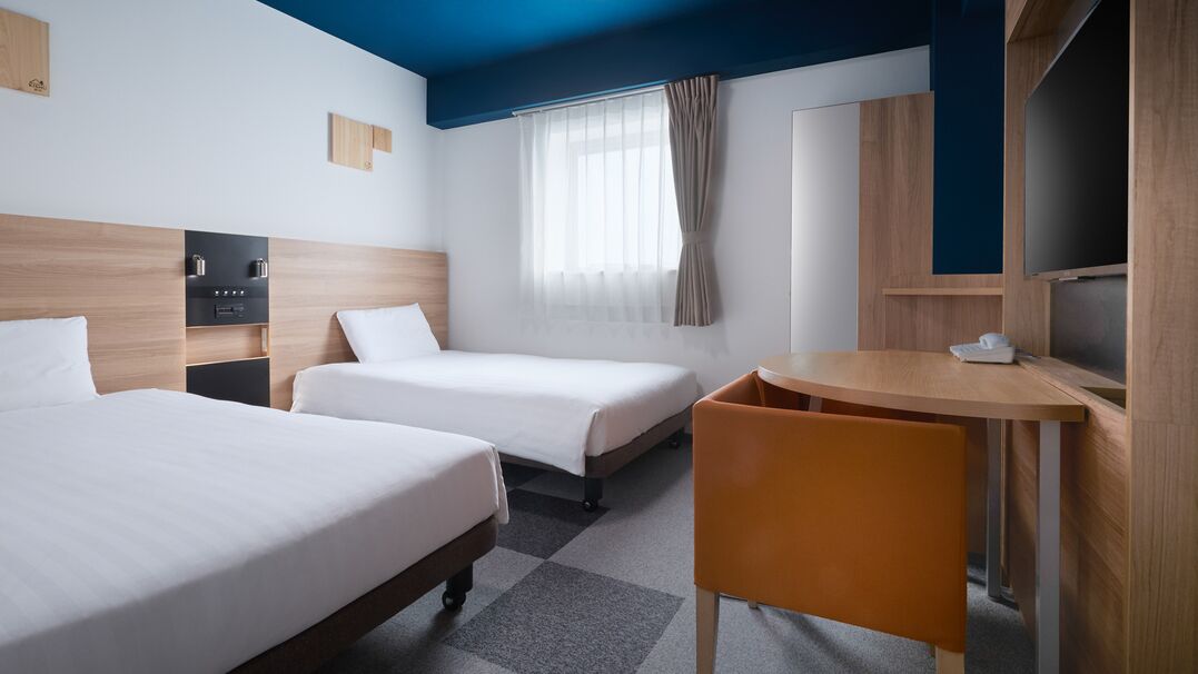 Une chambre d’hôtel avec deux lits, un bureau, une chaise, une télévision et une fenêtre avec des rideaux.