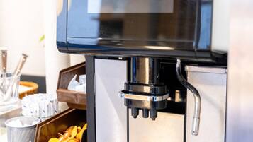 A coffee machine with a label, a metal container with orange peels, and a metal mesh trash can.