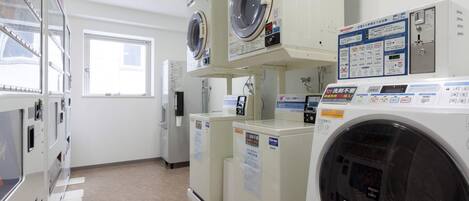 Un cuarto de lavandería con varias lavadoras y secadoras, un dispensador de agua fría y un ventanal que proporciona luz natural.