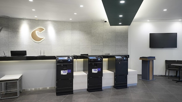 A reception area with a modern design, including a reception desk, a large illuminated logo, a flat-screen TV, and a seating area. - Comfort Hotel Wakayama (Wakayama)