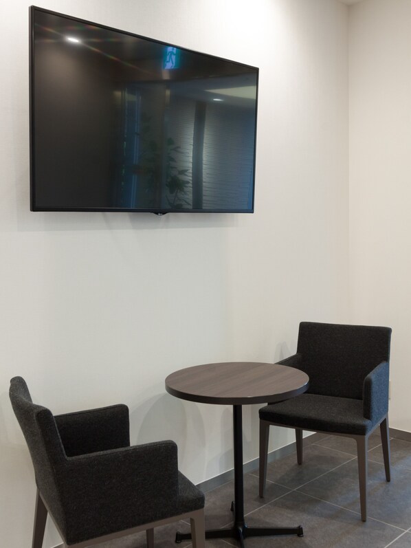 A room with a flat-screen TV mounted on the wall, two grey upholstered chairs, and a round table. - Comfort Hotel Wakayama (Wakayama)