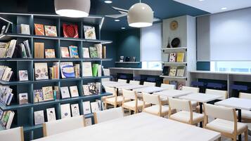 A library with bookshelves, tables, chairs, and pendant lights.