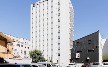 A tall hotel building with multiple floors and balconies, surrounded by parked cars and other buildings.