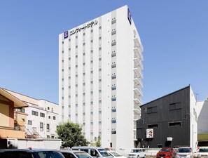 Un edificio de hotel alto con varios pisos y balcones, rodeado de automóviles estacionados y otros edificios.
