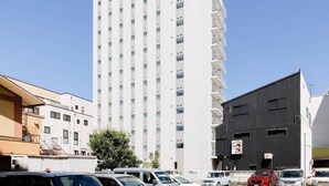 Un edificio de hotel alto con varios pisos y balcones, rodeado de automóviles estacionados y otros edificios.