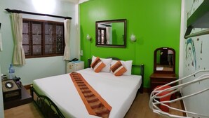 Habitación de hotel con cama, mesita de noche, espejo, ventana con cortinas y pared verde.