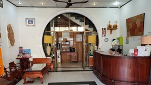 Vestíbulo de hotel con una recepción, zona de estar y vistas a la cocina y el comedor a través de un vidrio.