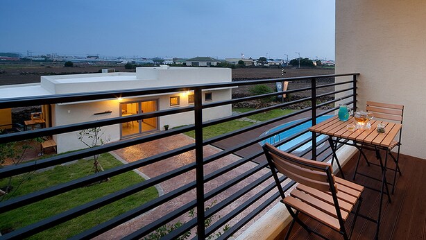 Een balkon met uitzicht op een modern huis, een zwembad en een eethoek met houten meubels.
