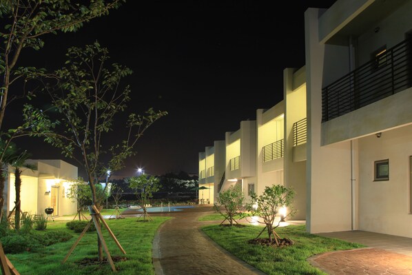 A pathway leading to a building with multiple balconies and a well-lit entrance.