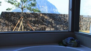 Een badkamer met een badkuip, een stenen muur en uitzicht op een berg.