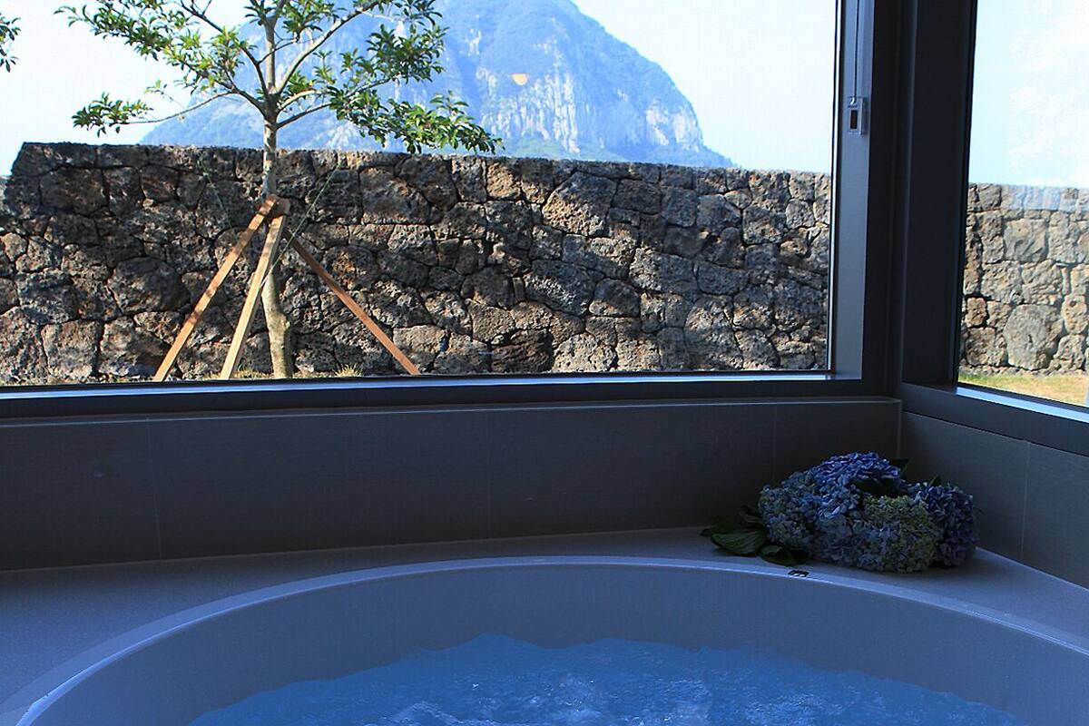 A bathroom with a bathtub, a stone wall, and a view of a mountain.