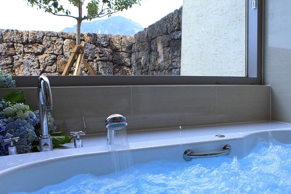 A bathtub with running water, a window, and a stone wall in the background.