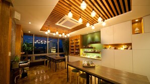 Een modern restaurant met houten vloeren, een lange houten tafel en hangende hanglampen.