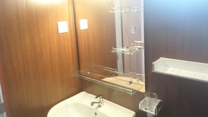A bathroom with a wooden vanity, a glass shelf, a sink, and a mirror. - Pradeepa Guest House (Polonnaruwa)
