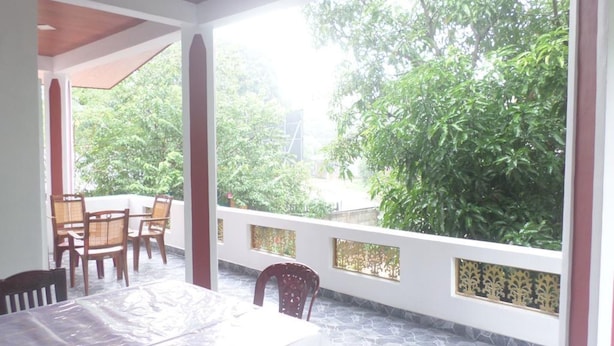 A covered outdoor dining area with a table and chairs, surrounded by a white wall with decorative panels, and a view of lush greenery. - Pradeepa Guest House (Polonnaruwa)