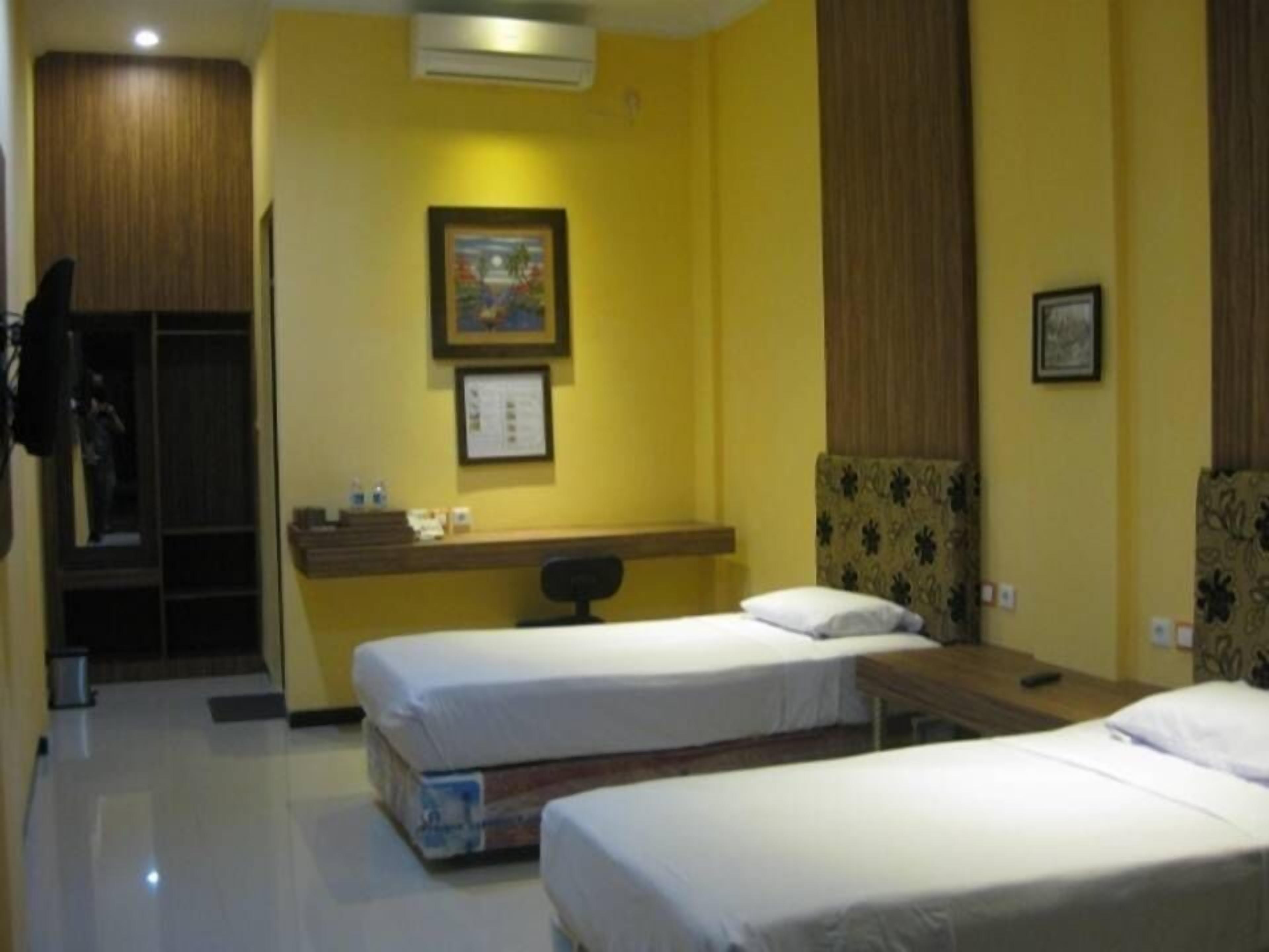A hotel room with two single beds, a desk with a chair, a mirror, and a framed picture on the wall.